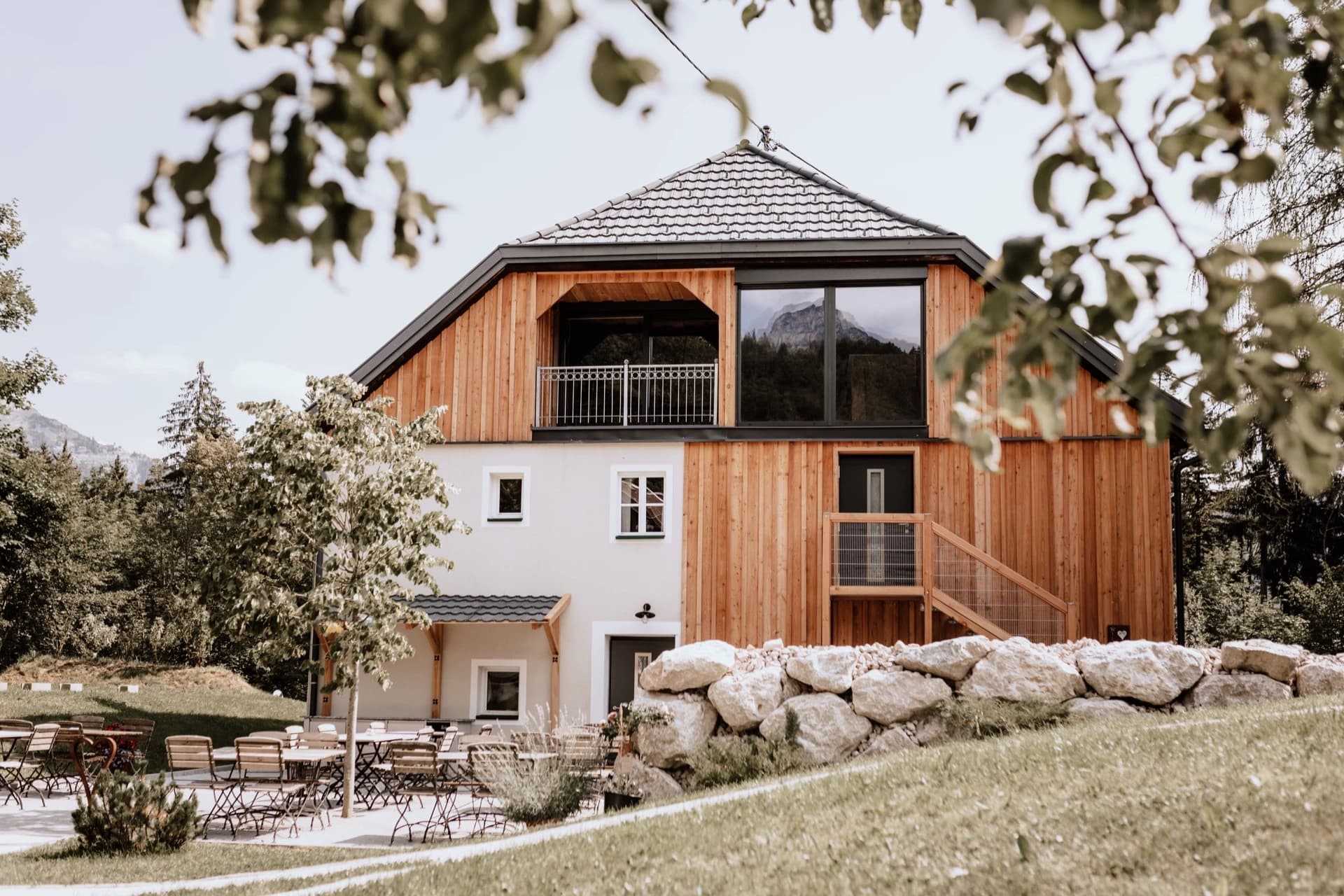 Modernes Chalet mit Holzfassade, großer Fensterfront und einer Außenterrasse inmitten einer grünen Berglandschaft.